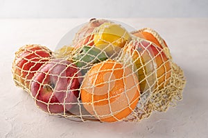 Bunch of mixed organic fruit, vegetables and greens in a string bag on light background. Zero waste add ecology concept