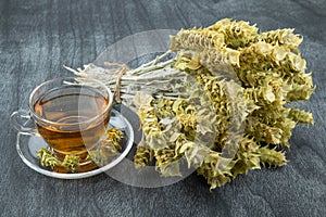 Bunch of mountain tea Malotira and mug with hot tea. Mountain tea sideritis. Natural Greek herbs on dark wooden background