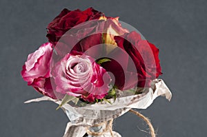 Bunch of multicolor rose flowers wrapped in newspaper over grey