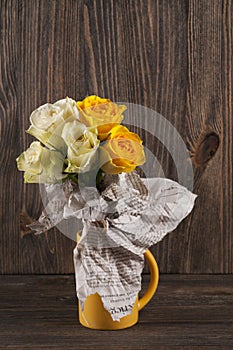 Bunch of multicolor rose flowers wrapped in newspaper over woode