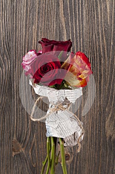 Bunch of multicolor rose flowers wrapped in newspaper over wooden background.