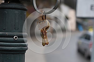 Bunch of old, rusty metal keys in key ring hanging on hook. Blurry town background