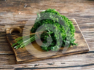 Bunch of raw fresh green curly parsley on wooden cut board on dark wooden background