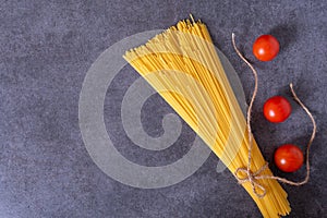 Bunch of raw Italian pasta with cherry tomatoes isolated on stone grey background.