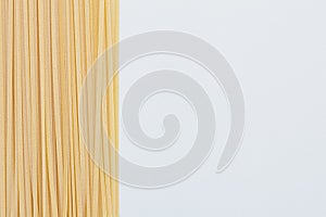 Bunch of raw linguine pasta on left side of white background