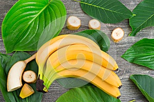 Bunch of raw organic yellow bananas with slices and green leaves on wooden background