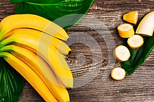 Bunch of raw organic yellow bananas with slices and green leaves on wooden background