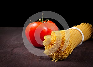 Bunch of raw pasta spaghetti with tomato on wood table