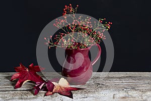 Bunch of red berries on the table in a red vase.