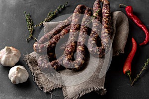 Bunch of red dry homemade sausage on a dark background and sackcloth, side view