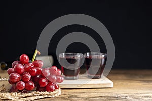 A bunch of red grapes with red grape juice in a glass placed on a wooden table or red wine, delicious natural healthy juice drink