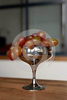 A bunch of red ripe juicy grapes in a metal bowl on a wooden table. Food, healthy eating. Soft selective focus