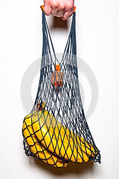 Bunch of ripe bananas in a handmade cotton bag on a white background.