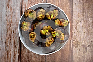 A bunch of ripe mangosteen fruits in a white bowl, on wooden table top