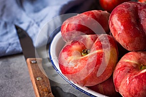 Bunch of ripe organic colorful red saturn peaches with water drops on white plate, knife, blue napkin, dark kitchen table