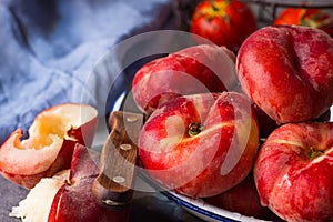 Bunch of ripe organic colorful red saturn peaches on white plate, halved, knife, blue napkin