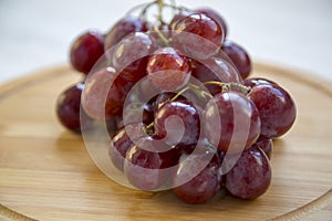 Bunch of ripe red grape on a round bamboo board.