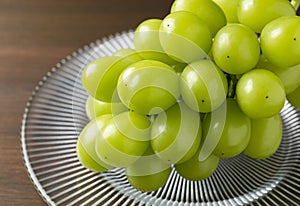 Bunch of Shine-Muscat grapes on a plate set against a wooden background