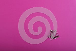 A bunch of silver safety pins of different sizes and shapes as the main object against a bright pink textured background.