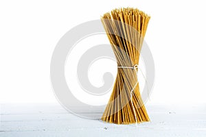 Bunch of standing wholemeal spaghetti on white wood, high key sh