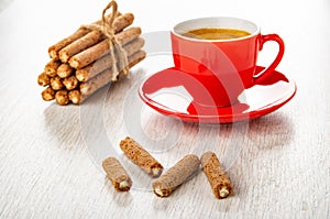 Bunch of sticks with cream filling, cup with coffee espresso on saucer, broken sticks on wooden table