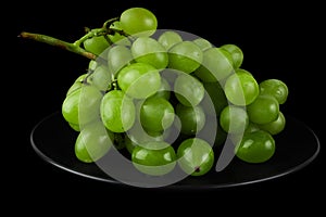A bunch of table grapes, white pouring, on a black plate, on a black background