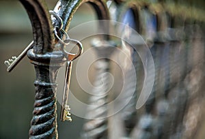 A bunch of two metal old vintage door keys hanging on a cast-iron fence of artistic casting in a park with a blurred background