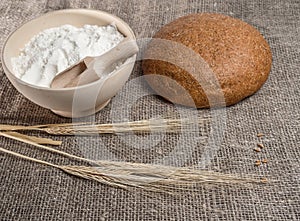 Bunch of wheat ears, a bowl of flour and round bread.