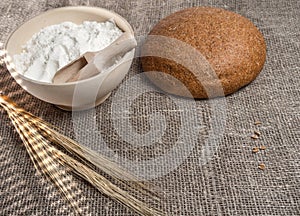 Bunch of wheat ears, a bowl of flour and round bread.