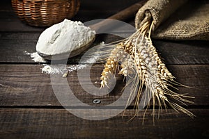 Bunch of wheat ears and wooden spoon with flour on wooden rustic table.