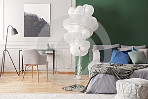 Bunch of balloons in elegant grey and green bedroom interior with king size bed with grey bedding, blue pillows and moss