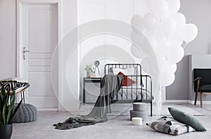 White balloons next to single metal bed with grey bedding and white and dark red pillows in bright scandinavian bedroom