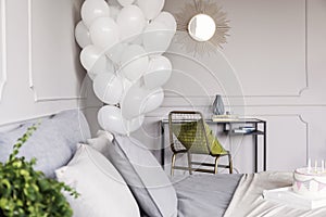 Bunch of balloons in trendy bedroom interior with industrial dresser with golden mirror and chair with green pillow and bed