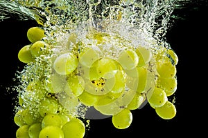 Bunch of white grapes splashing into clear water isolated against black background. Food splash photography