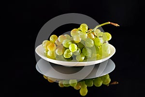 Bunch of white grapes on white plate isolated on a black glossy background