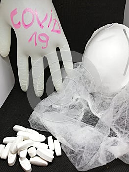 A bunch of white pills,medical cap,medical face masks,medical glove where written corona virus on a black and white background