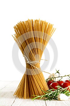 Bunch of wholemeal spaghetti standing on white wood with some to