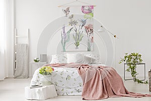 A bunch of yellow fresh cut flowers in a bright bedroom interior with a bed dressed in white linen and peach blanket. Fabric on th