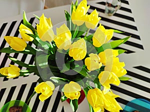 A bunch of yellow fresh tulips stabding in vase on dining table. View from above