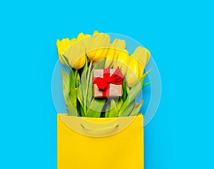 Bunch of yellow tulips and cute gift in cool shopping bag on th