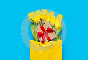 Bunch of yellow tulips and cute gift in cool shopping bag on th