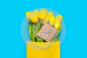 Bunch of yellow tulips and cute gift in cool shopping bag on th