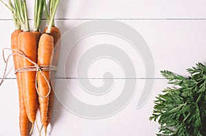 Bunch of young carrots with green tops on white wooden vintage table, healthy food on mock up background top view