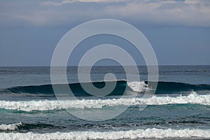 A bunch of young surfers surf at a popular location at Nyang Nyang Beach in Bali, Indonesia. Large waves break and form a thick