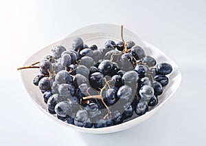 Bunches of blue grapes in white plate on white background. Berries, summer harvest, healthy eating