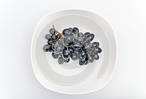 Bunches of blue grapes in white plate on white background. Berries, summer harvest, healthy eating