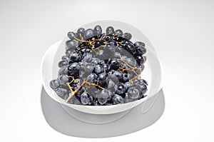 Bunches of blue grapes in a white plate on a white background. Berries, summer harvest, healthy eating