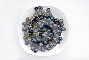 Bunches of blue grapes in a white plate on a white background. Berries, summer harvest, healthy eating