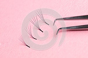 Bunches of fake lashes and tweezers on pink background. Eyelash extension procedure