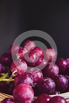 Bunches of purple and red grapes in a wicker basket on a dark background. The harvest of unwashed grapes in a basket. Ecologically